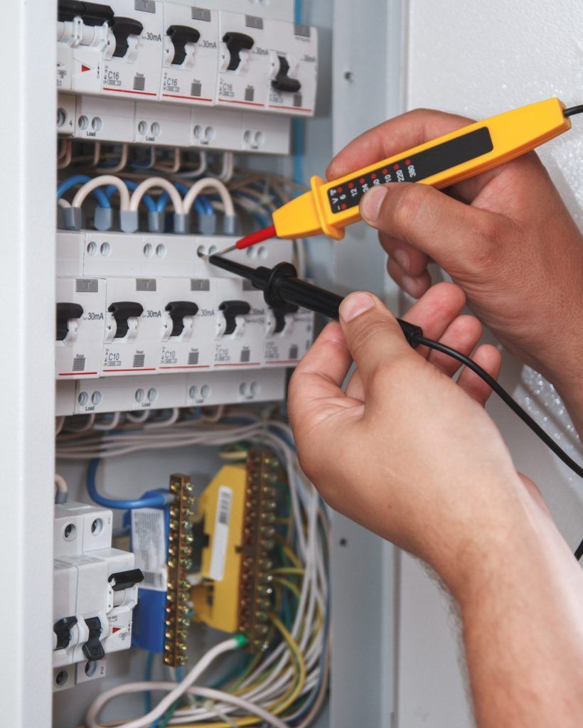 Hands of electrician with multimeter probe at an electrical switchgear cabinet examining fuse box